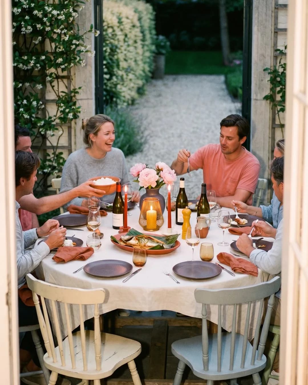 Un groupe d'amis profitant d'un dîner autour d'une table dressée dans un jardin à Knokke, avec bougies, fleurs et vin.