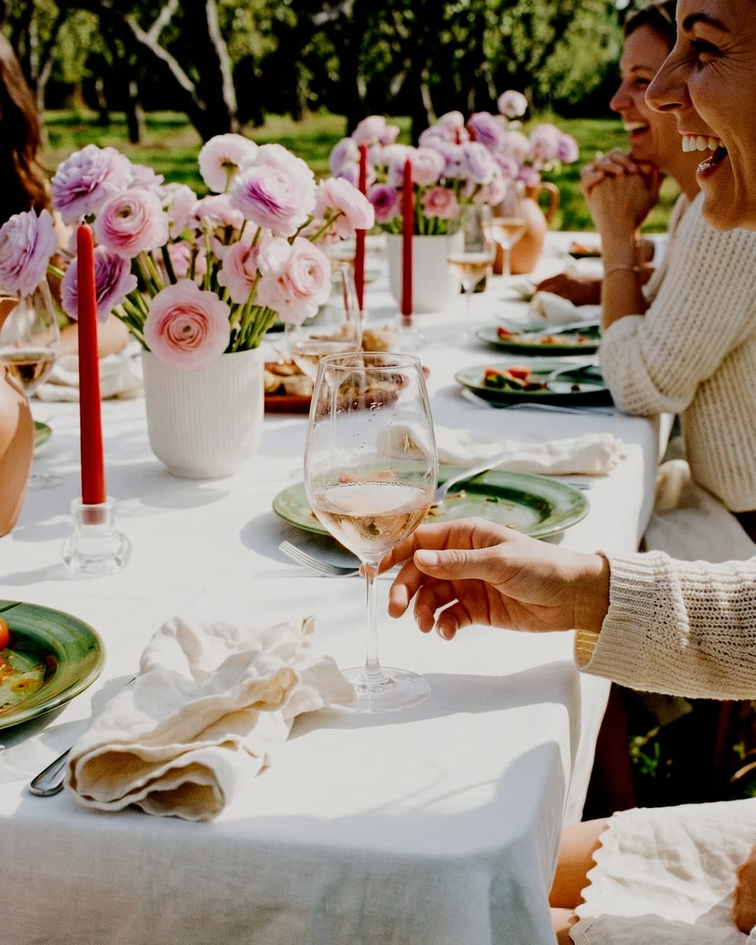 Table d’anniversaire baignée de soleil, dressée sur une terrasse face à la mer, avec fleurs, fruits, vin et plats à partager