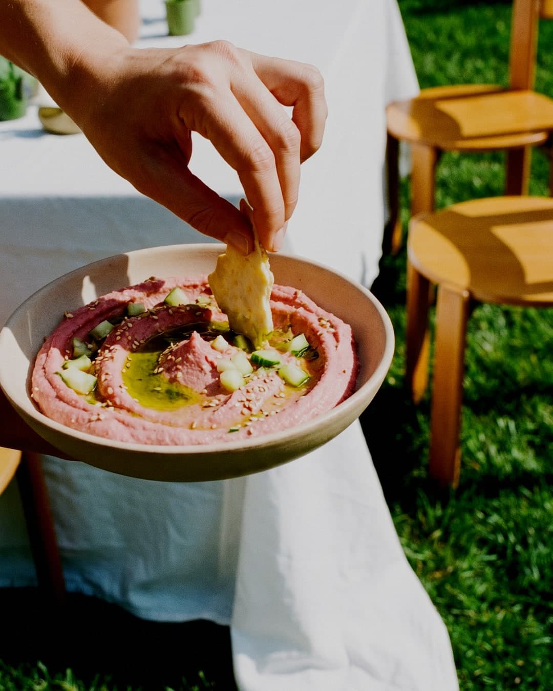 Hand dipping a cracker into a bowl of pink beetroot spread at an outdoor table